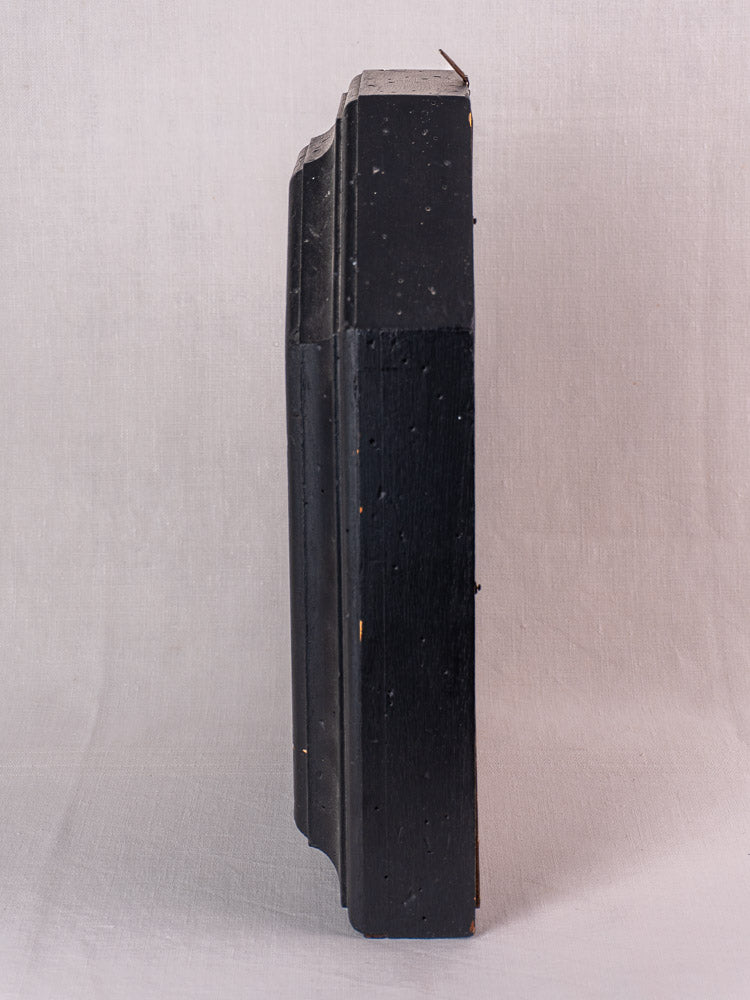 Antique French black painted wood wall clock with ornate edge, late 19th century, on light fabric.
