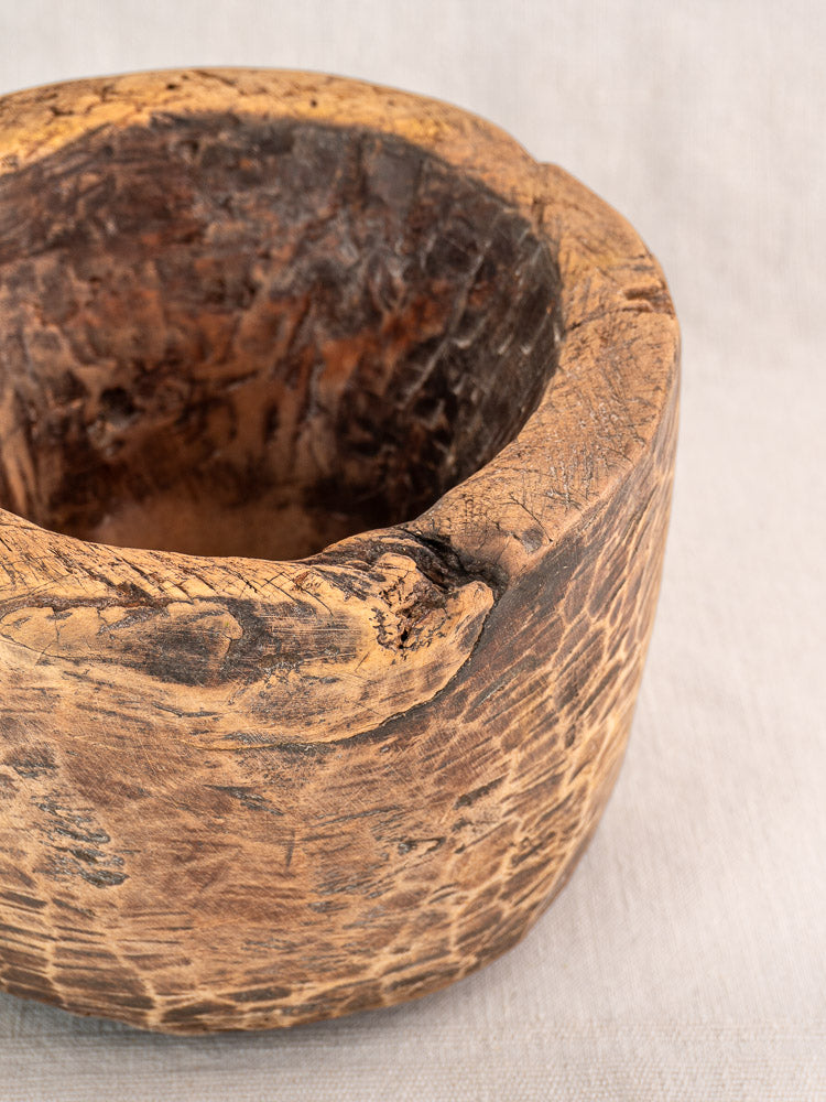 Antique French wooden mortar, late 18th–early 19th century, rustic round form on light fabric.