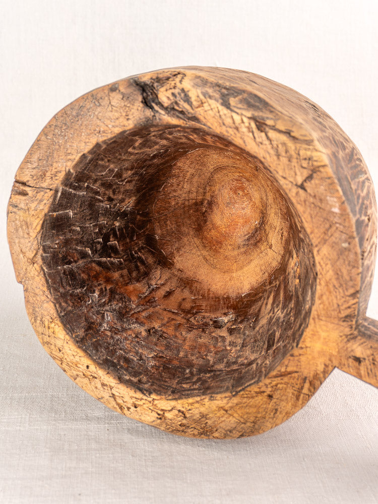 Antique French wooden mortar and pestle with hand-carved bowl, rustic texture, light fabric background.