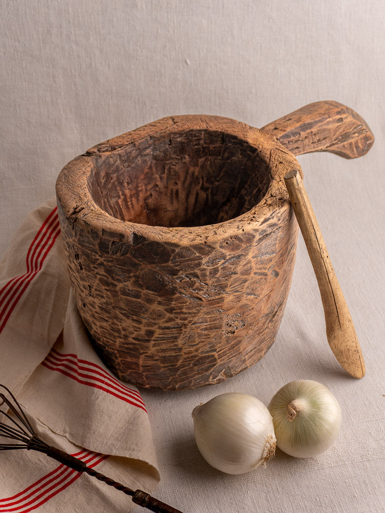 Antique French wooden mortar and pestle on beige cloth with white onions and striped towel.