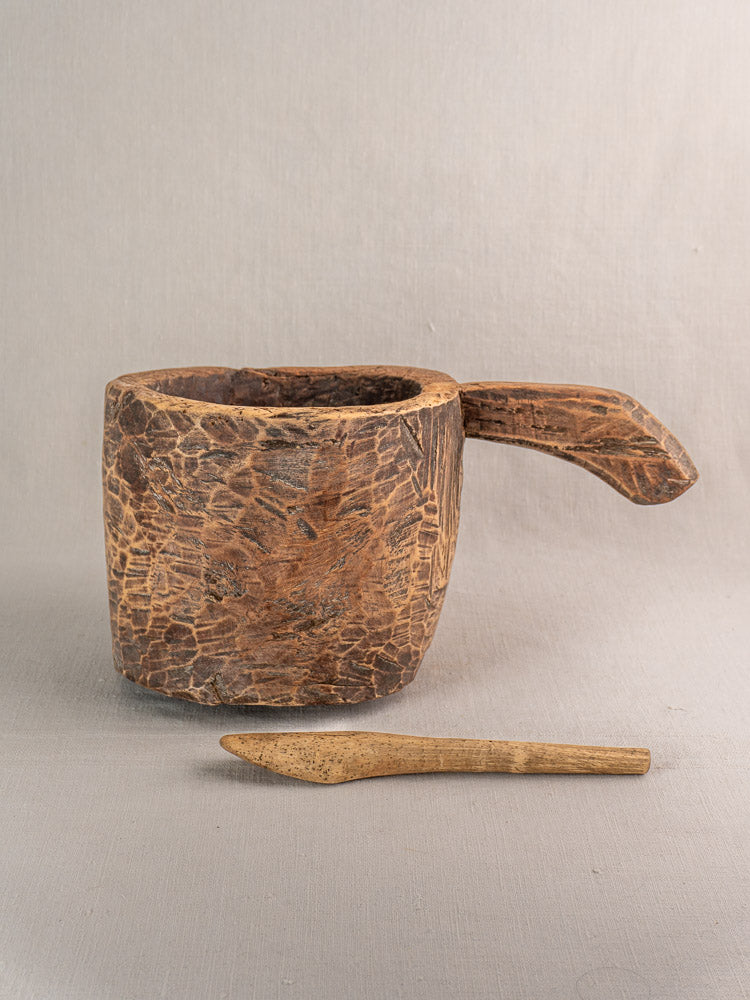 Antique French wooden mortar and pestle, hand-carved with aged patina, on gray surface.