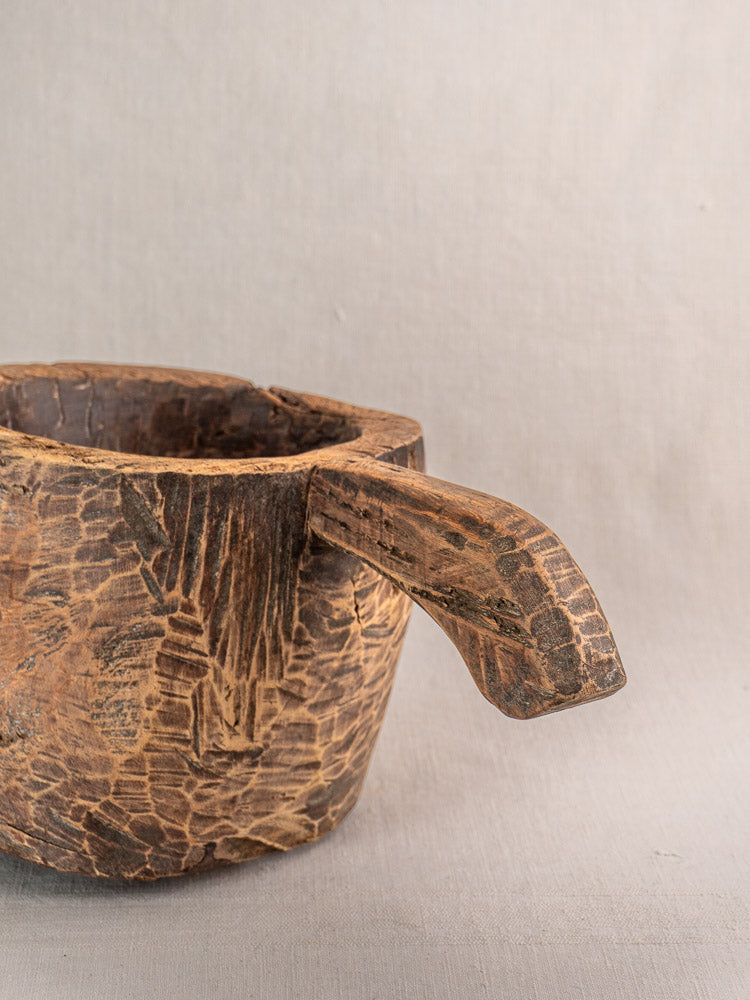 Antique French wooden mortar and pestle, hand-carved with rustic texture, on neutral fabric background.