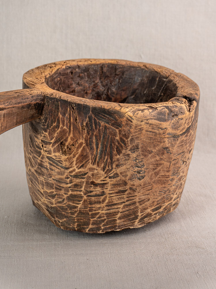 Antique French wooden mortar and pestle, hand-carved with rustic texture, set on light gray fabric.