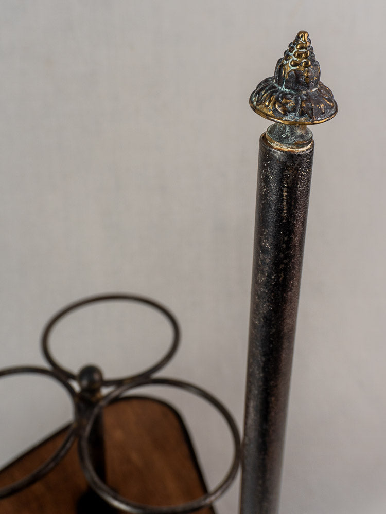 Antique French bottle carrier with wrought iron holders and decorative finial on a wooden base.