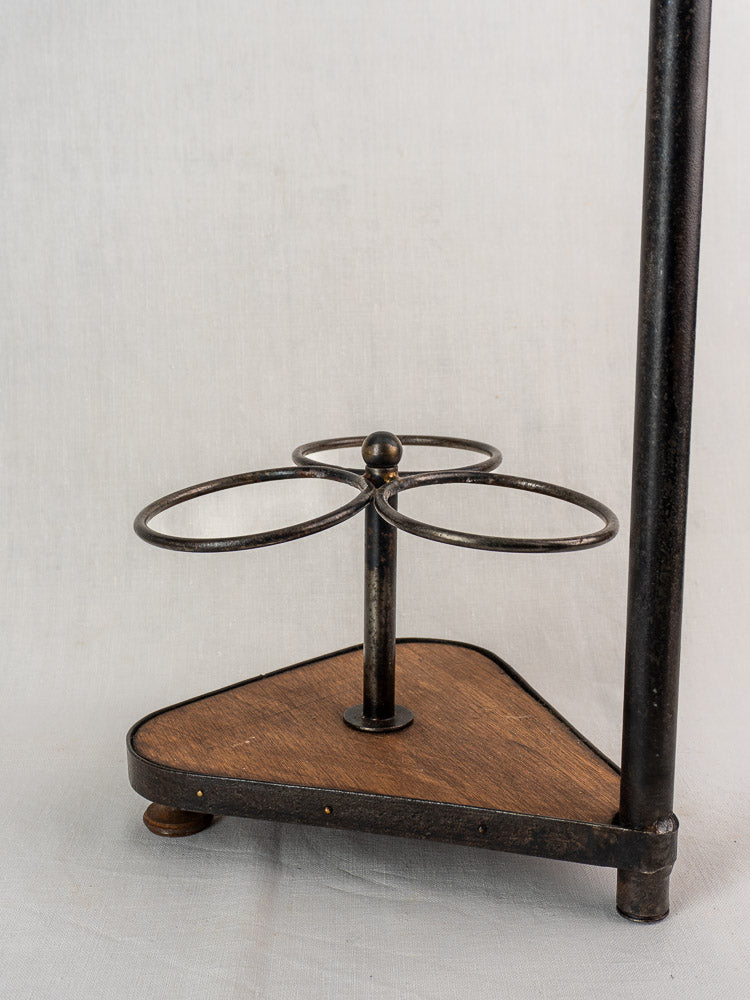 Antique French bottle carrier with three wrought iron holders on triangular wood base, plain background.