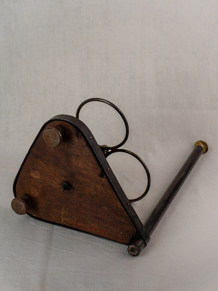 Antique French wrought iron and wood bottle carrier with triangular base and two circular loops on plain background.