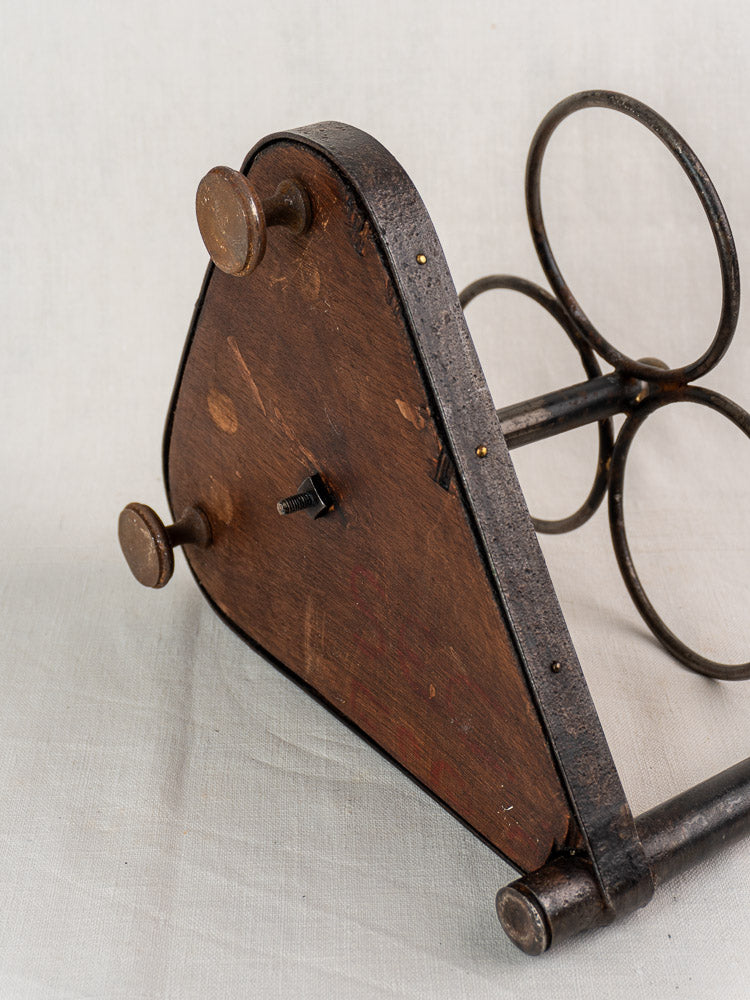 Antique French bottle carrier of wrought iron and wood, triangular base, on light fabric background.
