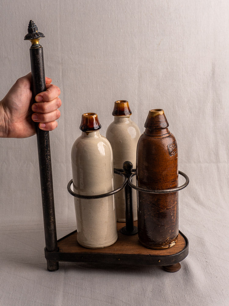 Antique French wrought iron and wood bottle carrier with three ceramic bottles, plain white background.