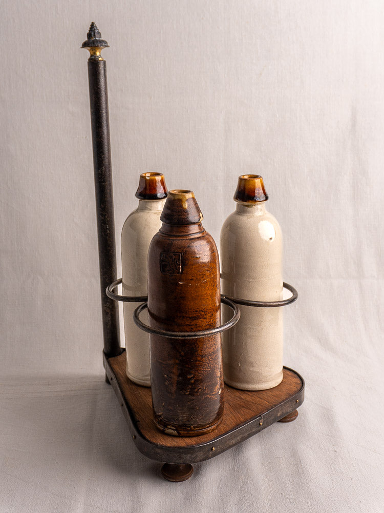 Antique French wrought iron and wood bottle carrier with three ceramic bottles on plain background.