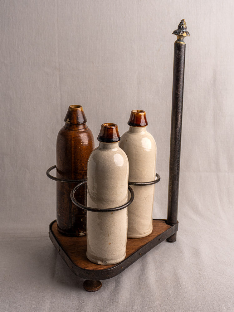 Antique French wrought iron and wood bottle carrier with three ceramic bottles on a wooden tray.