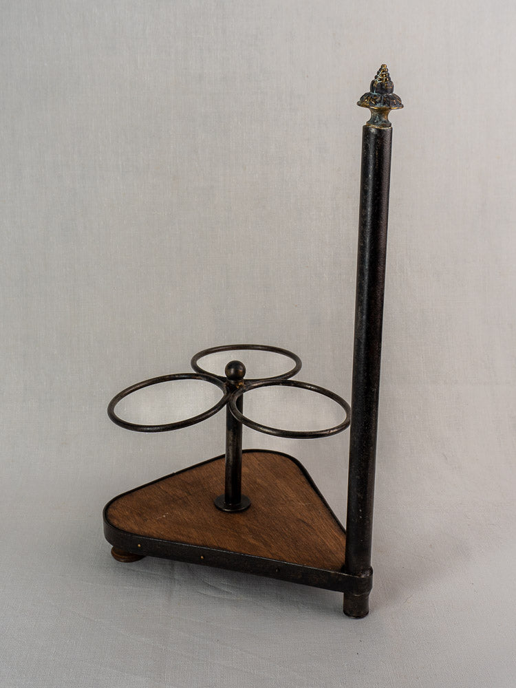 Antique French wrought iron and wood bottle carrier with three holders and a finial, on plain background.