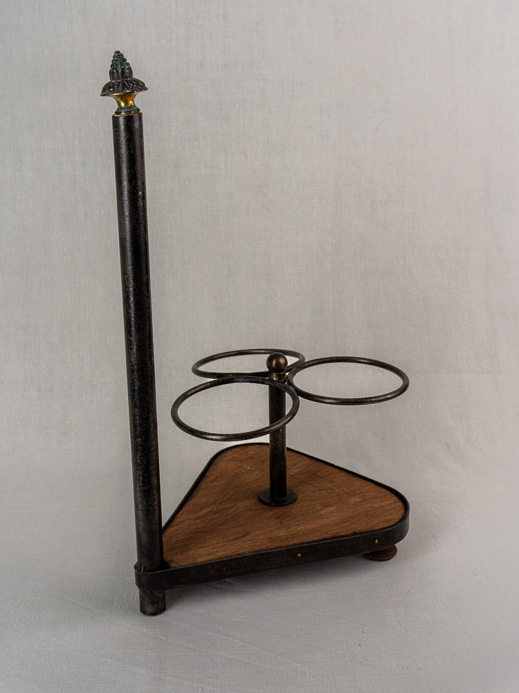 Antique French wrought iron and wood bottle carrier with three holders and decorative finial, on light gray background.