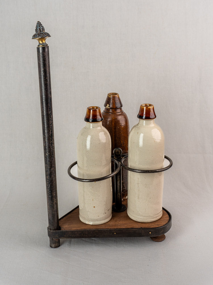 Three ceramic bottles in a French wrought iron and wood bottle carrier with tall vertical handle on white background.