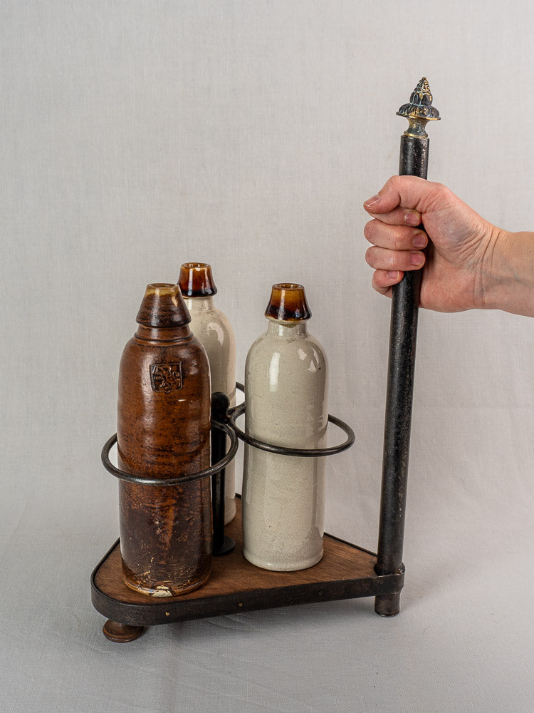 Antique French wrought iron and wood bottle carrier with three ceramic bottles, plain white background.
