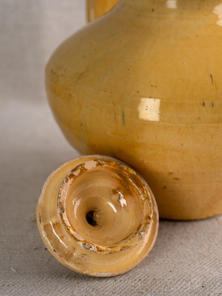 Antique French yellow-glazed Provençal earthenware teapot and lid on a neutral fabric surface.