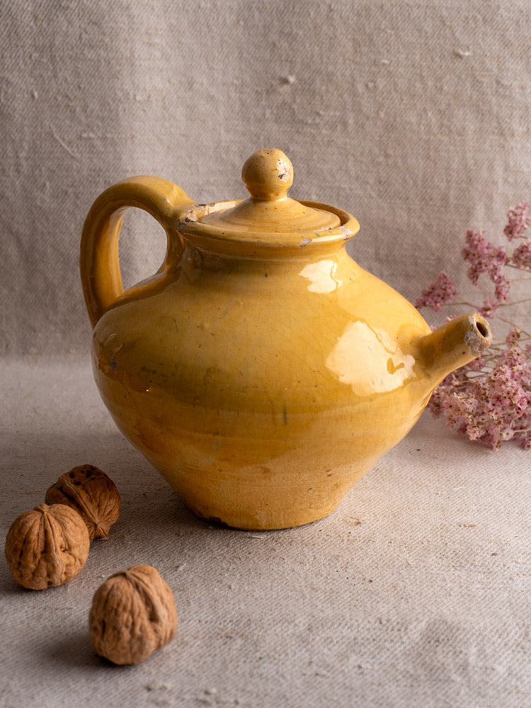 Antique French yellow glazed teapot with round lid and curved handle on beige fabric background.