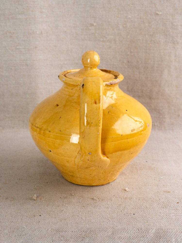 Antique French yellow glazed earthenware teapot with lid and handle on beige fabric background.