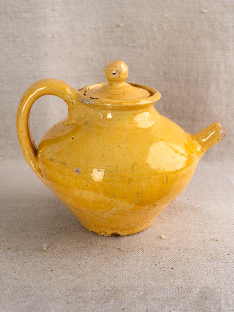 Antique French Provençal yellow glazed earthenware teapot with curved handle on neutral fabric background.