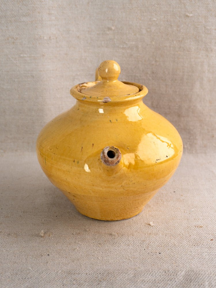 Antique French yellow glazed Provençal earthenware teapot with round lid and small spout on beige fabric.