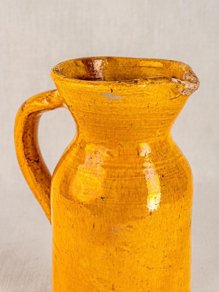 Antique French yellow glazed terracotta pitcher with handle and spout on a light background.