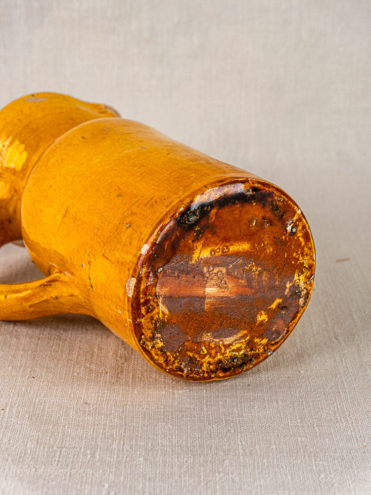 Antique French pichet jaune, 19th-century yellow glazed terracotta mug showing weathered base on light fabric.