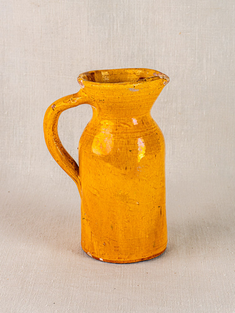 19th-century French yellow glazed terracotta jug with round body and curved handle on fabric background.