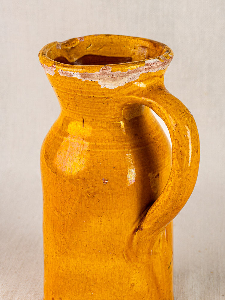 Antique French Pichet Jaune, 19th-century yellow glazed terracotta jug with chips, neutral background.