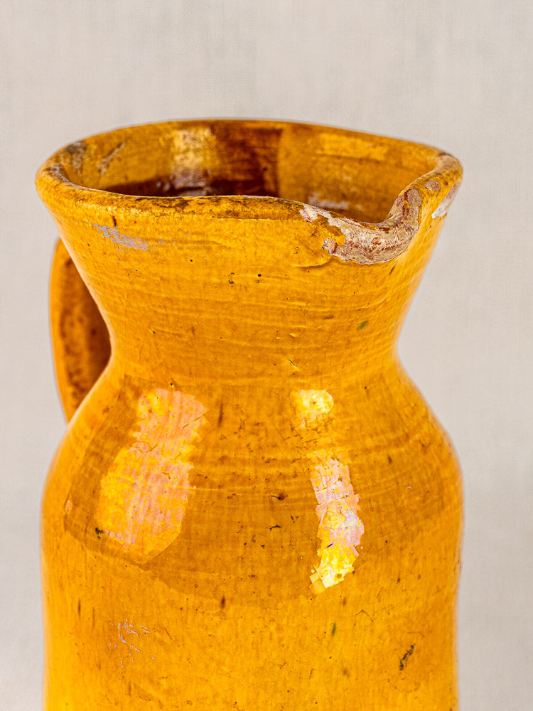 Antique French yellow glazed terracotta pitcher with chipped spout and glossy texture on neutral background.