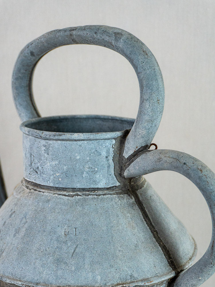 Antique French zinc broc à eau with blue-gray patina, twin curved handles, visible seams, plain light background.