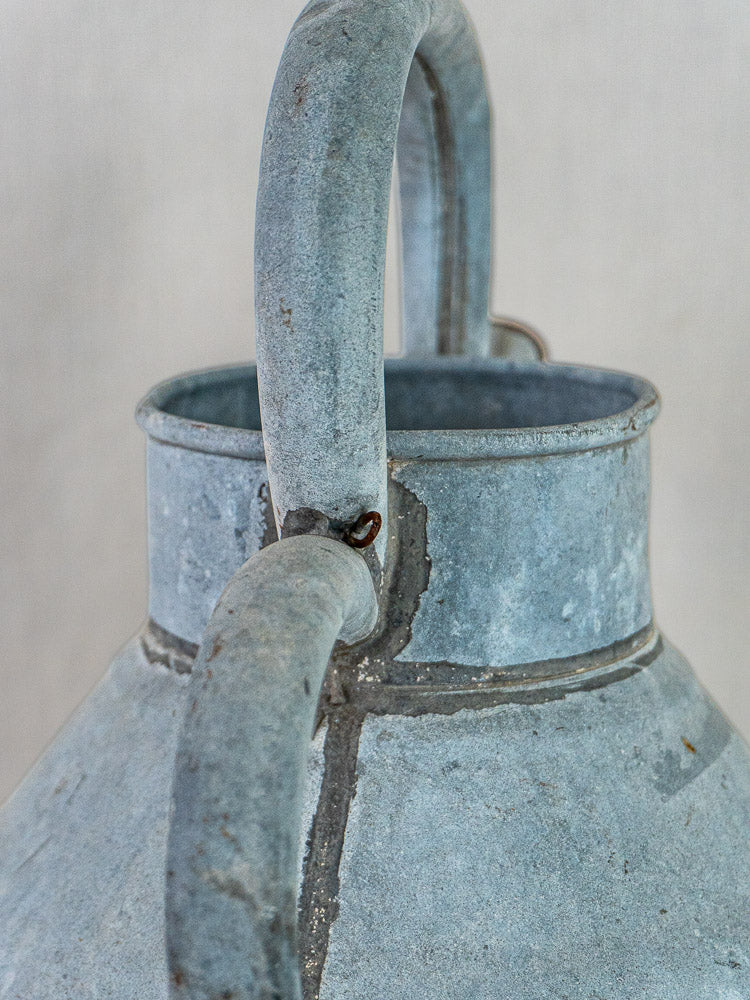 Antique French zinc broc à eau with blue-gray patina, curved handle, welded seams, and rust.