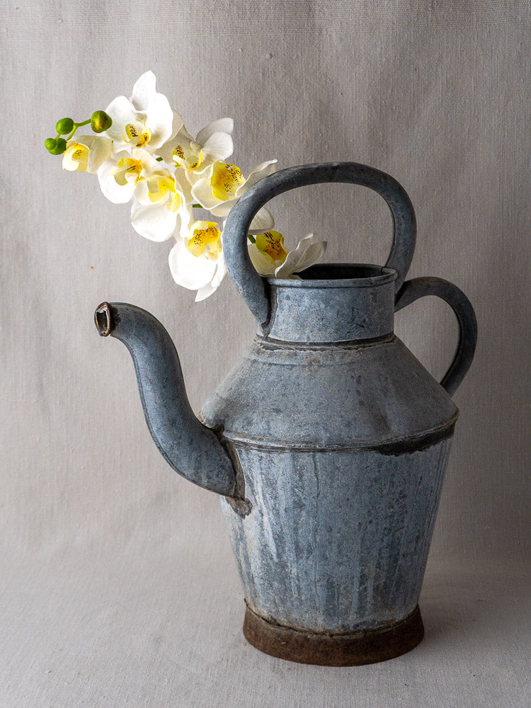 Antique French zinc water pitcher with blue-gray patina, large top handle, long spout on light background.