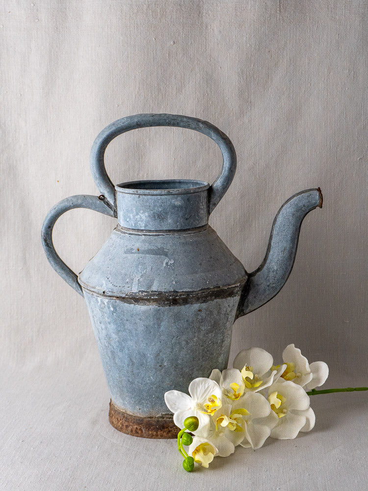 Antique French zinc broc à eau with blue-gray patina, displayed beside white orchid flowers.