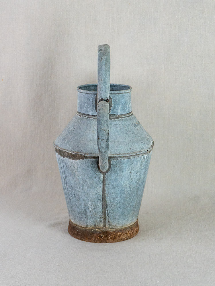 French zinc antique water pitcher with blue-gray patina and rusty handle on neutral fabric background.