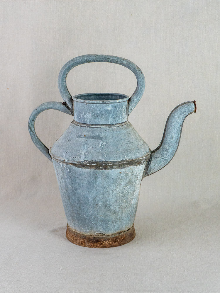 Antique French zinc water pitcher with blue-gray patina, large handles, and curved spout on fabric background.