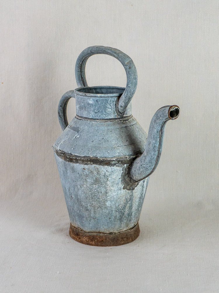 Antique French zinc water pitcher with blue-gray patina and top handle on a light surface.