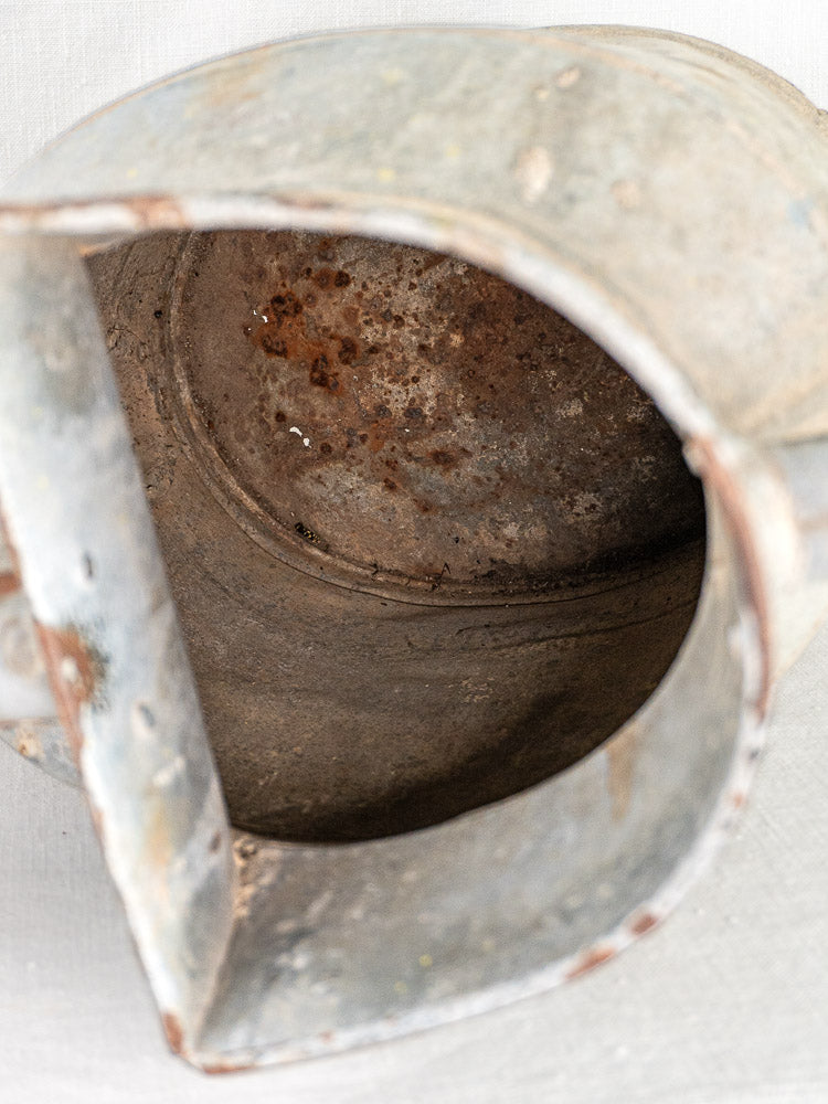 Large antique French zinc watering can with visible interior rust, spout and handle partially shown.