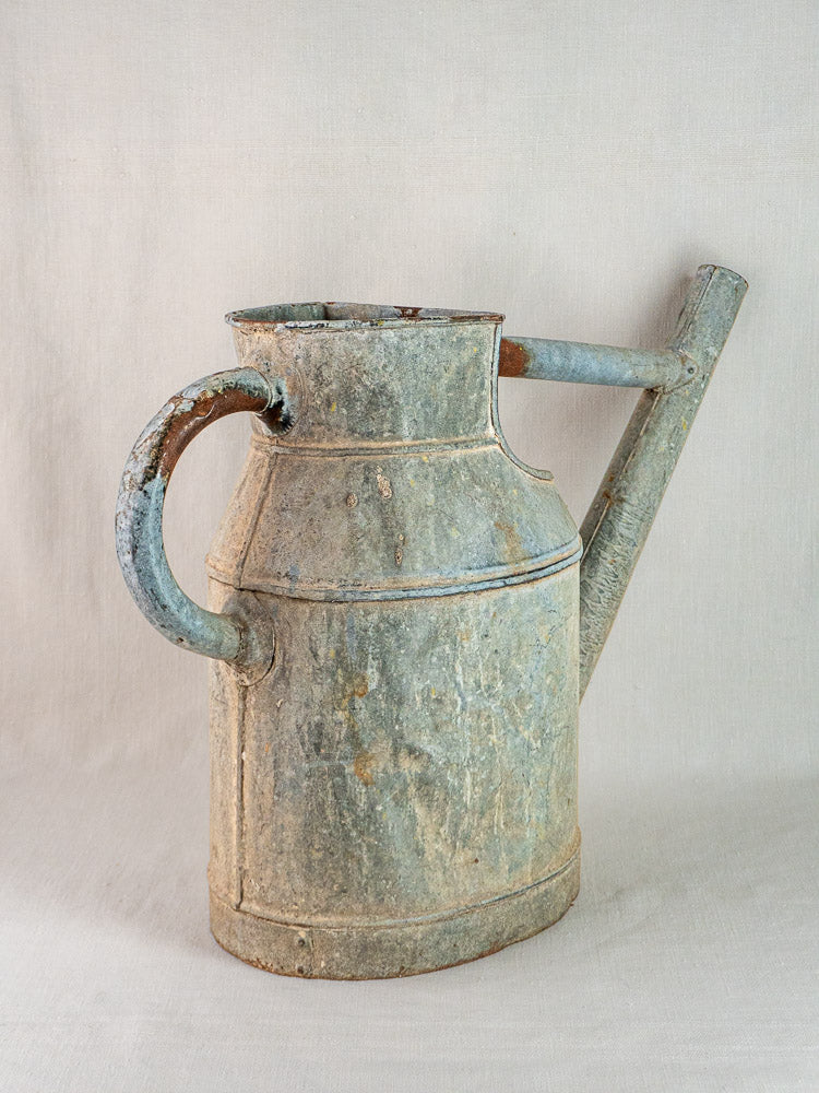 Large antique French zinc watering can with curved handle and long spout on neutral background.