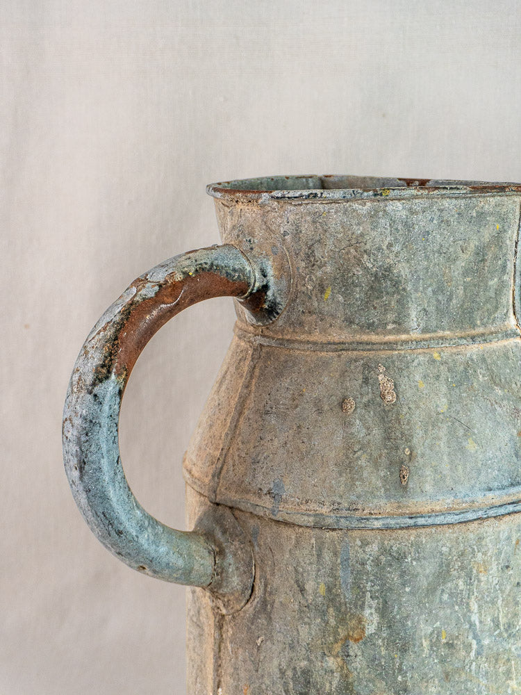 French antique zinc market garden watering can with curved handle, aged rust and patina, on light background.