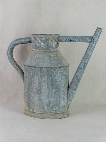 Antique French zinc watering can planter with curved handle and long spout on beige surface.