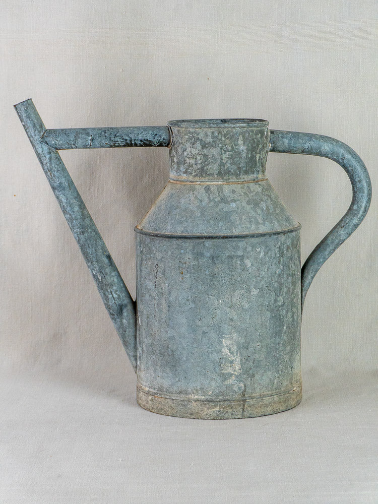 Antique French zinc watering can planter with long curved handle and spout on light surface.
