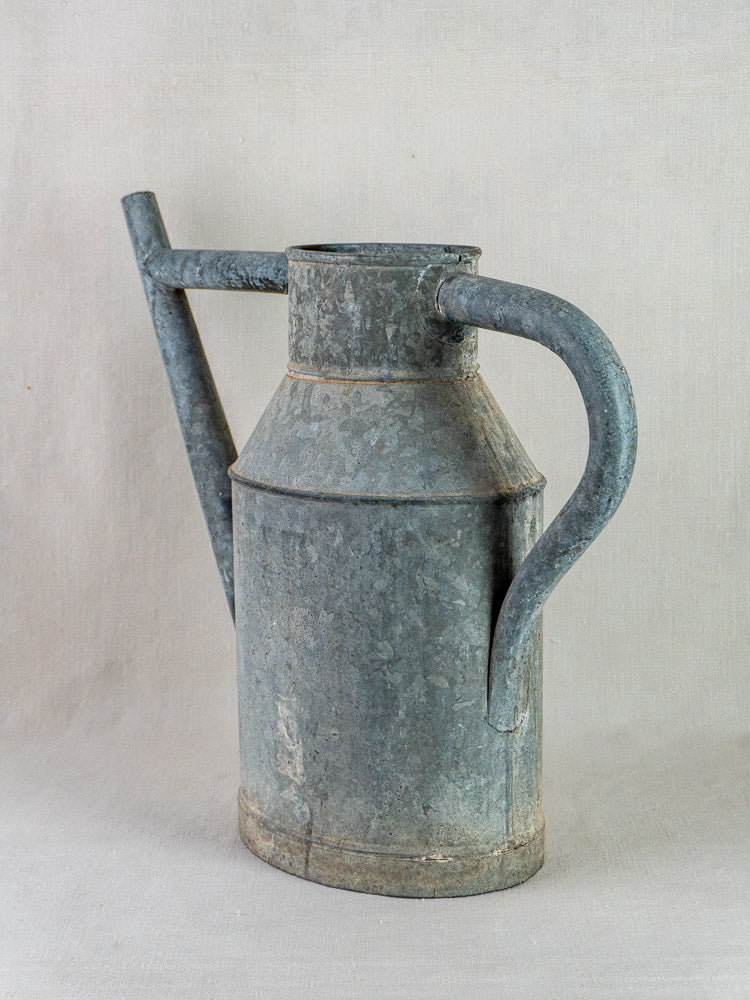 Antique French zinc watering can planter with long spout and large handle on light background.