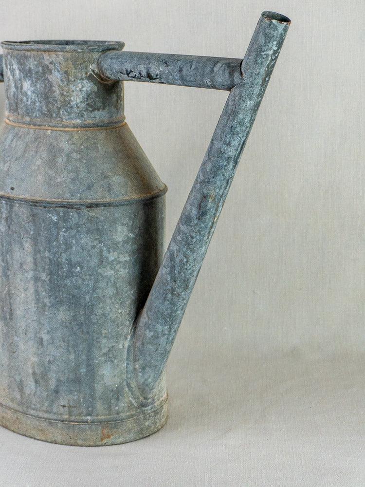 French zinc watering can planter with long spout and handle, partial view against neutral background.