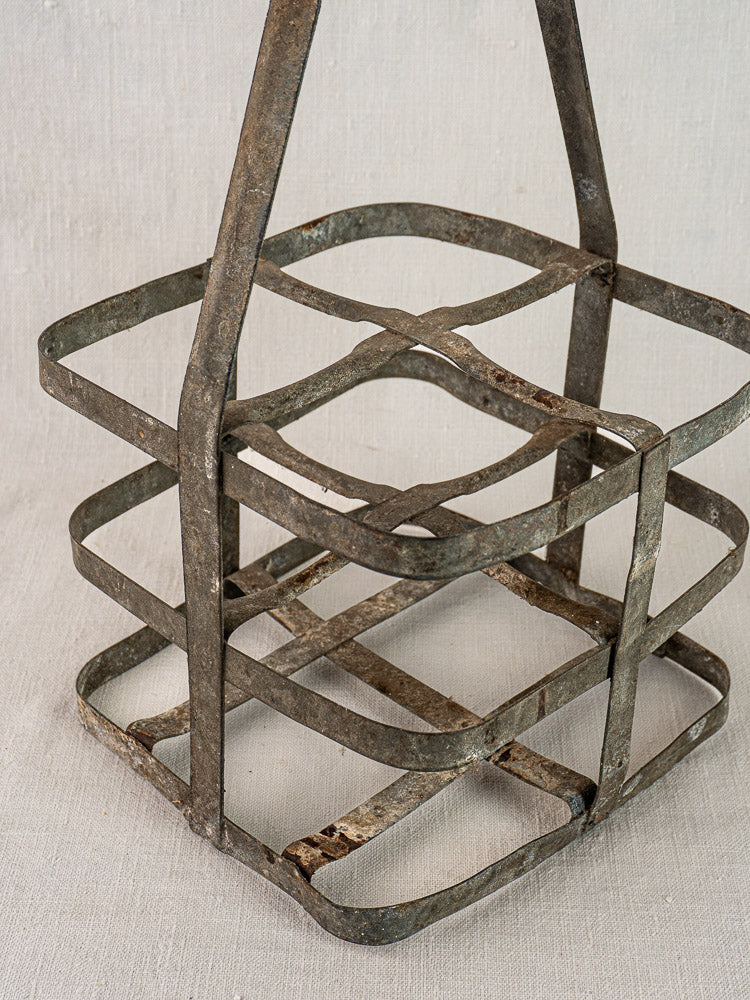 Antique French zinc and wood four-bottle wine carrier with rusted metal frame on light fabric background.