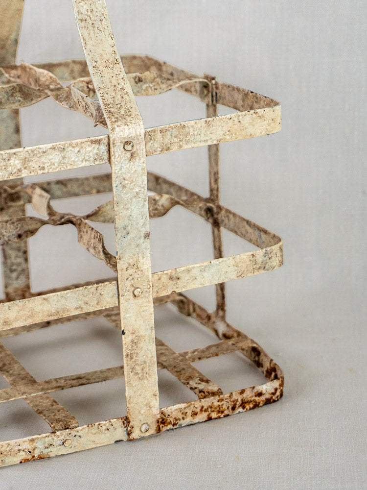 Antique French zinc four-bottle wine carrier with rustic white finish and rusted grid, neutral backdrop.