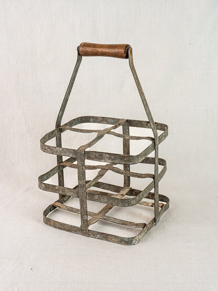 Antique French zinc and wood wine carrier for four bottles on a neutral fabric background.