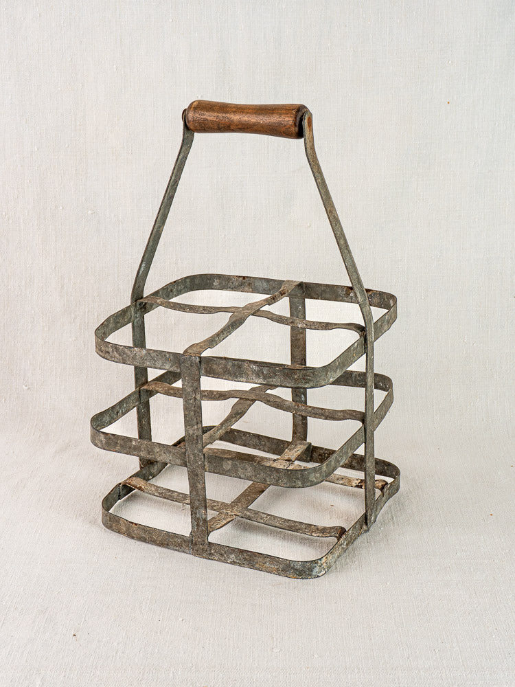 Antique French zinc and wood wine carrier for four bottles on a neutral fabric background.