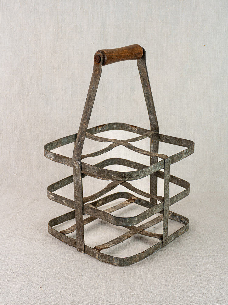 Antique French zinc and wood four-bottle wine carrier with rustic patina, on neutral fabric background.