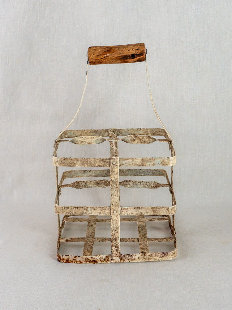 Antique painted zinc French wine carrier with wooden handle and four bottle compartments on a light background.