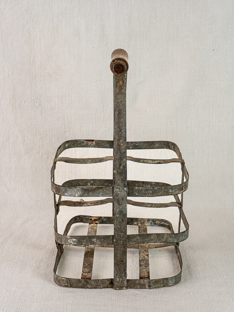 Antique French zinc and wood four-bottle wine carrier with metal frame and wooden handle on neutral fabric.