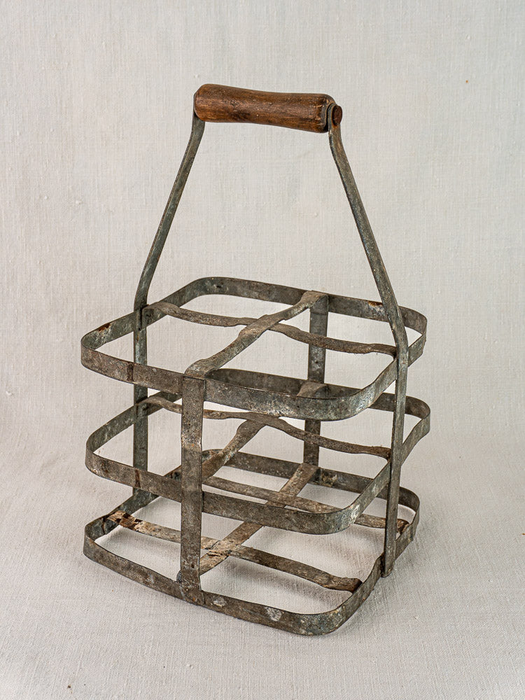 Antique French zinc and wood wine carrier with four-bottle metal frame and wooden handle on light fabric background.